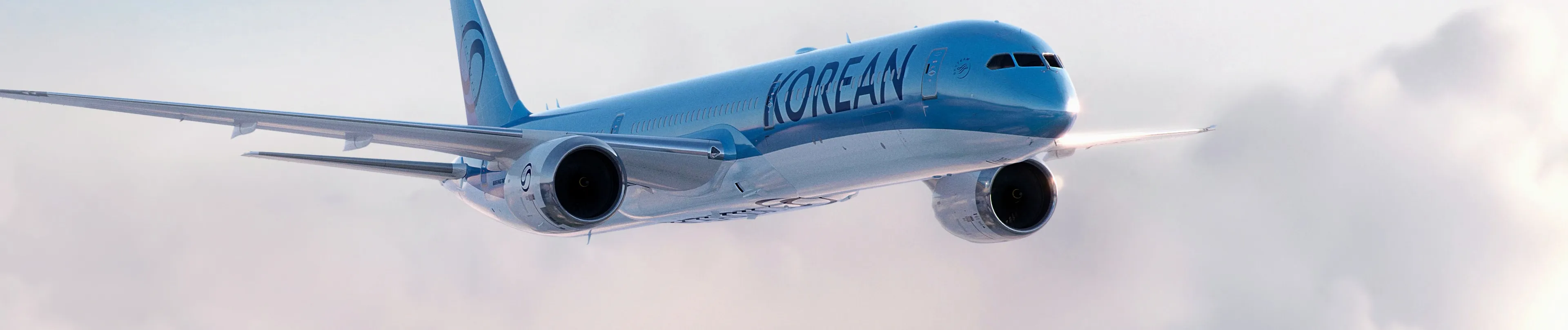 Boeing 787-10 Korean Air během letu ve výšce nad oblaky. Pohled zprava zepředu, s logem Korean Air na modrobílém trupu a motory pod křídly.