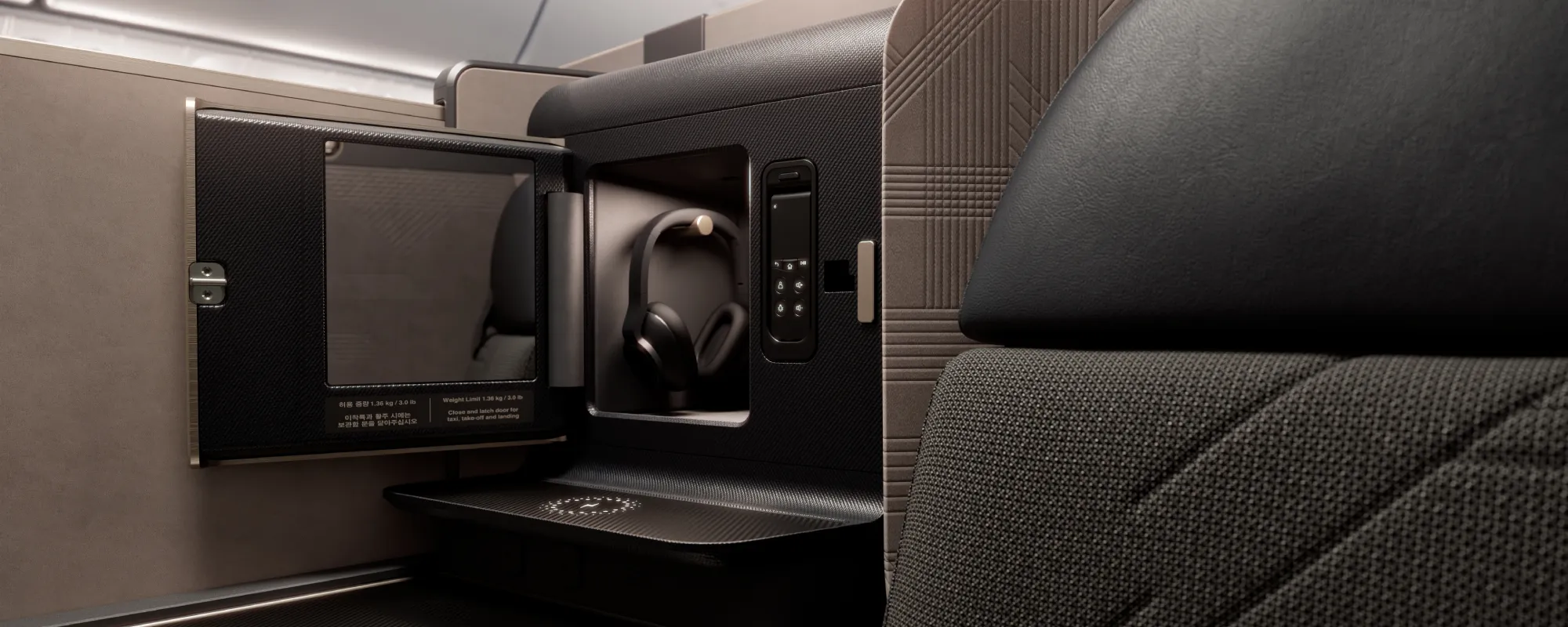 Detail úložného prostoru v sedadle Prestige Suite 2.0, s přihrádkou na sluchátka, ovladačem a uzavíratelnou skříňkou, integrovaný v bočním panelu sedadla.